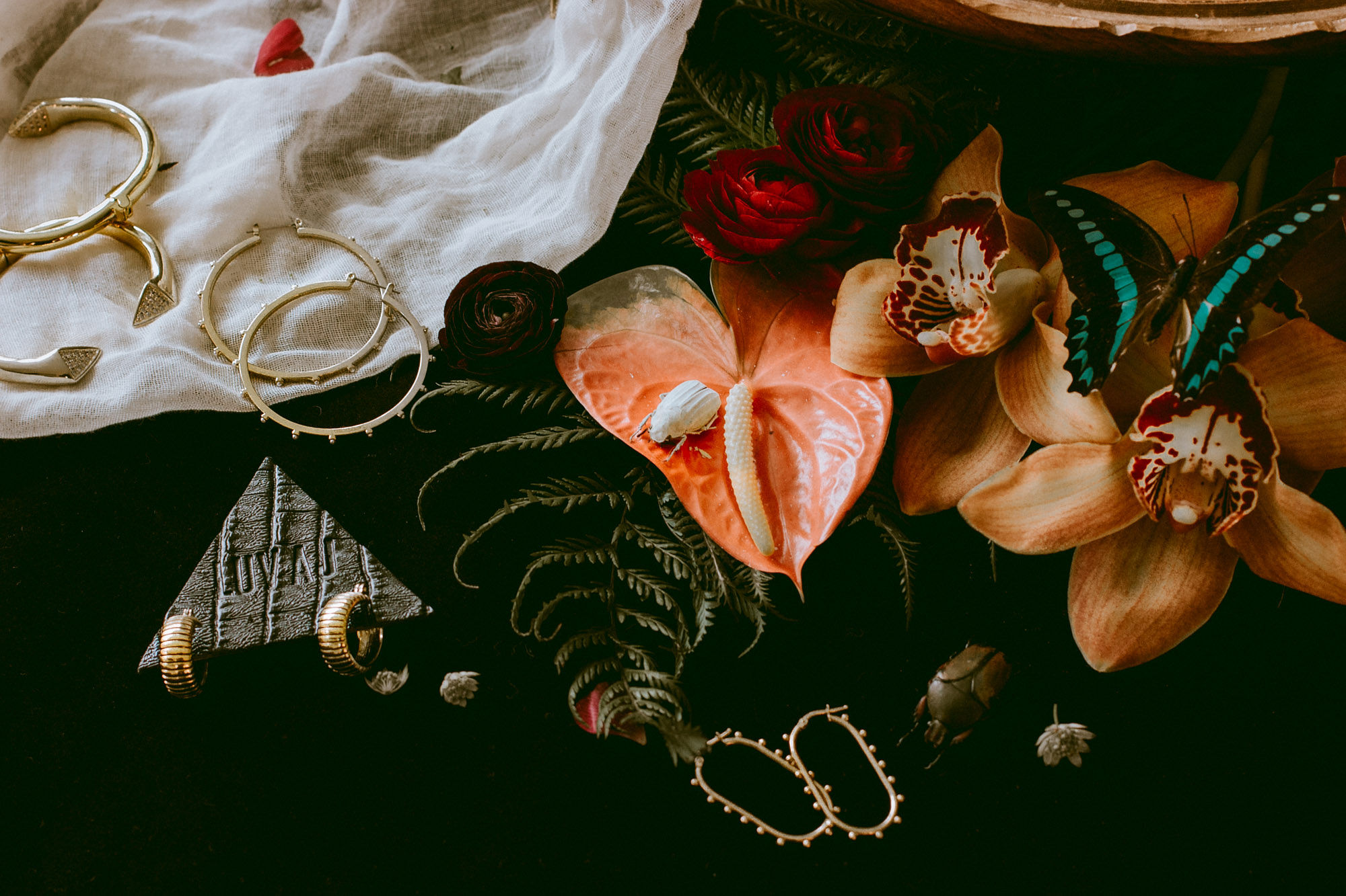 A dark editorial arrangement of jewelry pieces and flowers